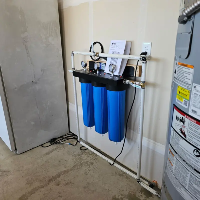 Close view of a three-stage whole-house water filter with pressure gauges above each blue housing