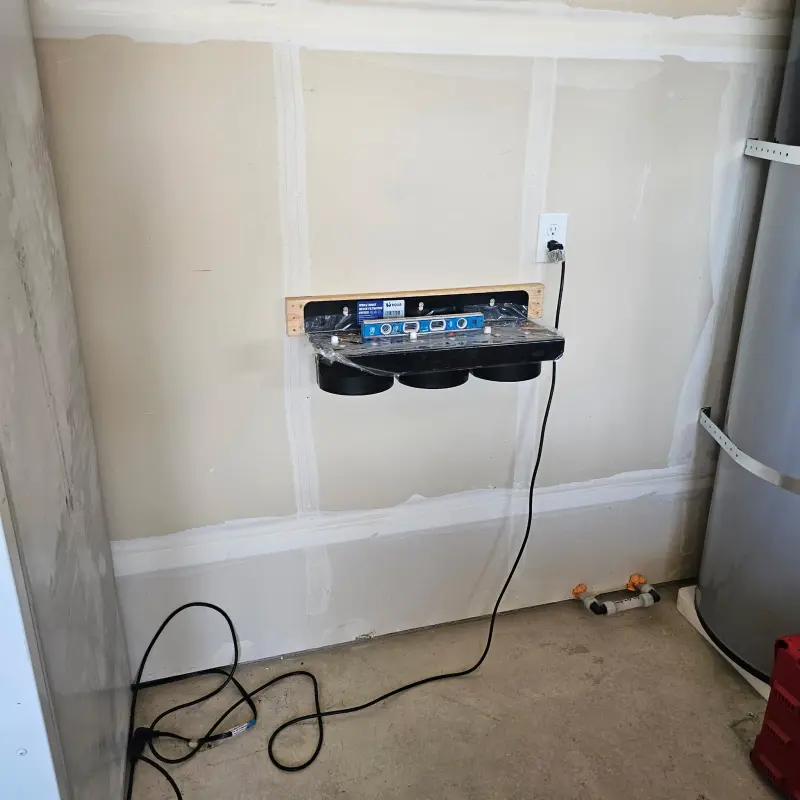 A bare three-stage filter manifold mounted and levelled on wood backing in a garage, not yet plumbed in