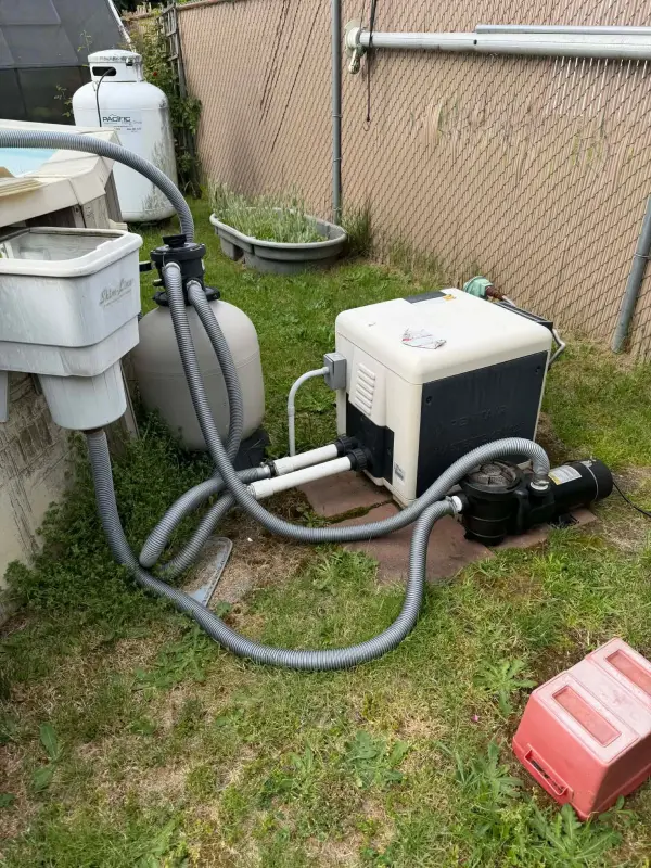 Propane pool heater connected to a sand filter and pump beside an above-ground pool