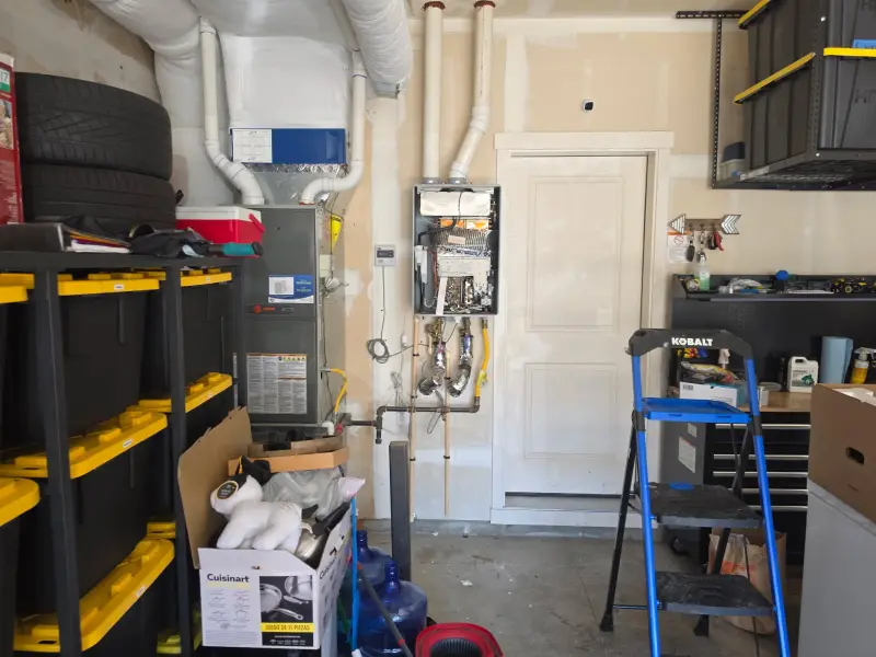Tankless water heater hung on the garage wall with its front cover off during installation