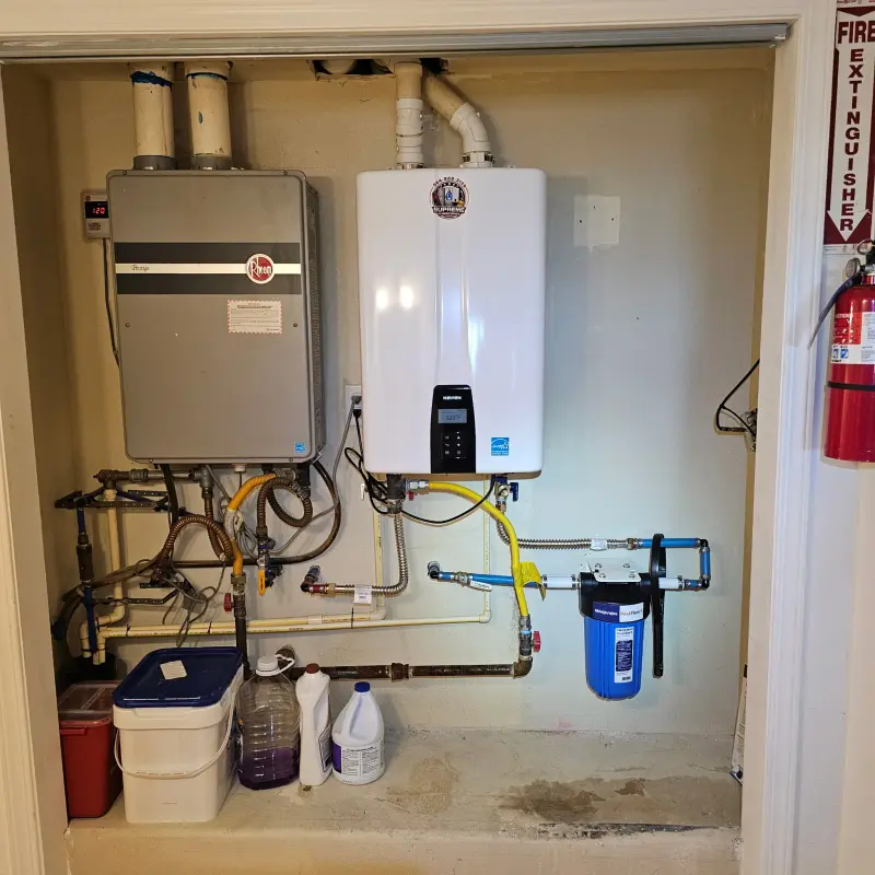 A new white Navien tankless water heater installed beside an existing unit, with a blue sediment filter plumbed in below
