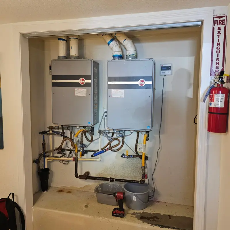 Two older Rheem tankless water heaters mounted side by side in a closet before replacement