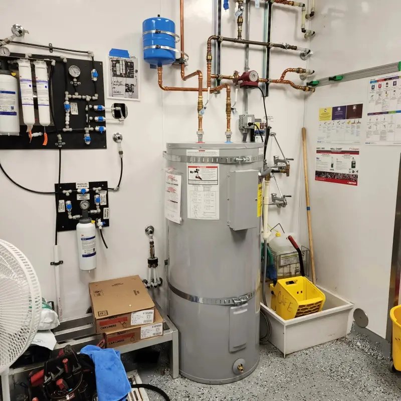 Commercial water heater installed in a cafe back room with copper piping and a recirculation pump