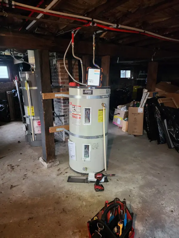 New water heater set and strapped in a basement mid-installation with the old unit alongside